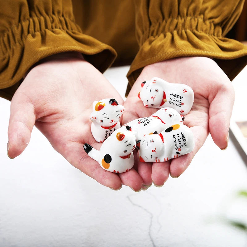 Hands holding small ceramic kawaii cat figurines with a blurred background