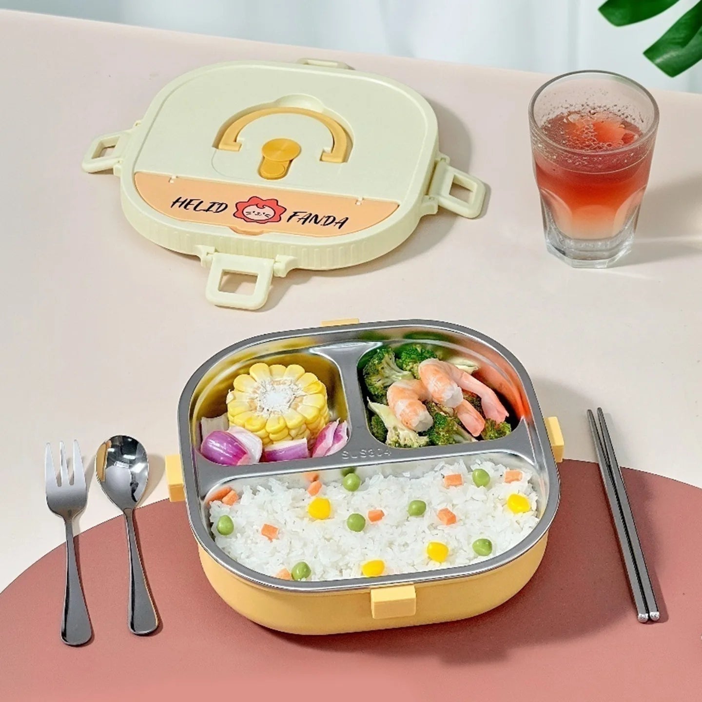 Colorful kawaii bento box with compartments of food, a glass of juice, utensils, and a pink mat.