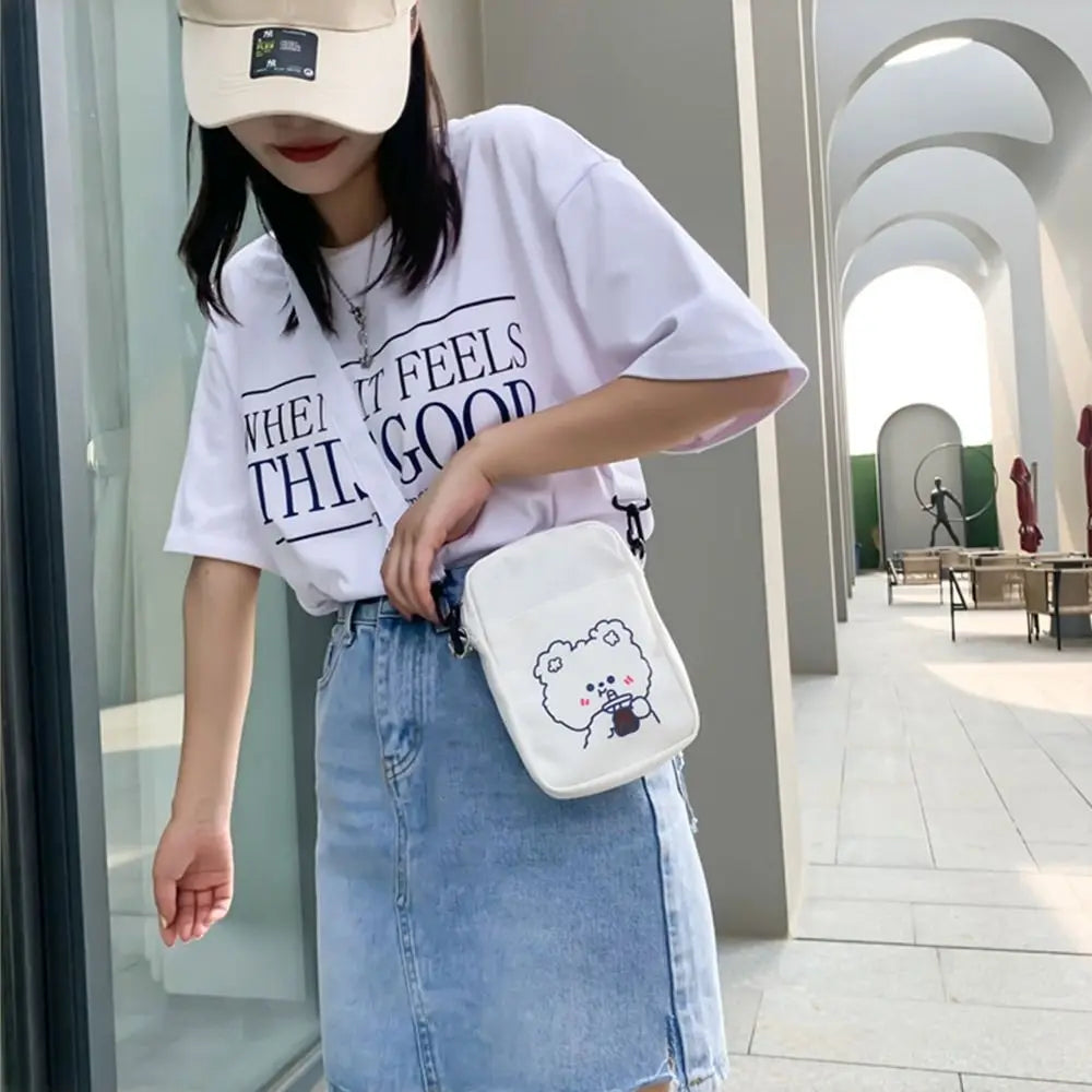 Person wearing a white t-shirt with text, blue jeans, and a white bag with a Kawaii cartoon design.