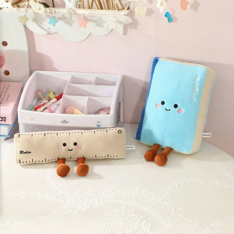 Two kawaii plush toys, a ruler and a blue pillow with a face, on a white surface.