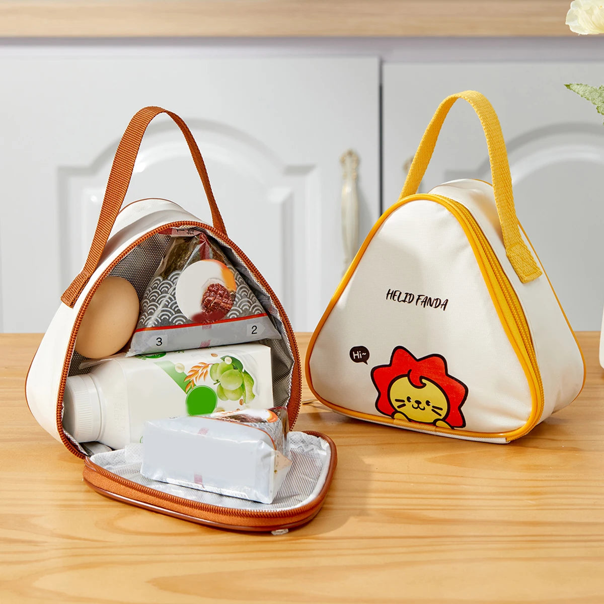 Two lunch bags, one open with contents, the other closed with a kawaii cartoon lion design, on a wooden surface.