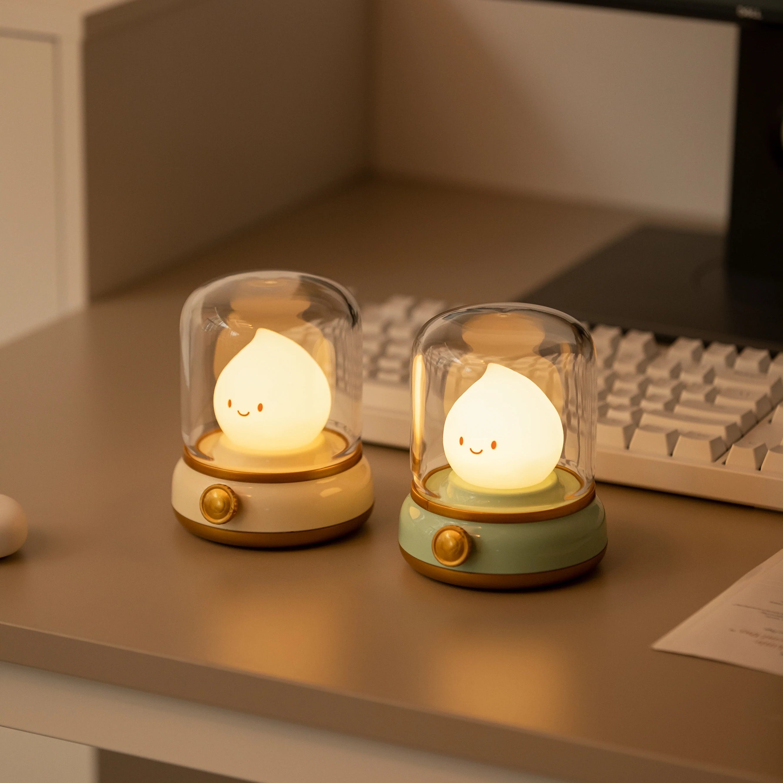 Two small, kawaii glowing lamps on a desk with a computer monitor in the background.