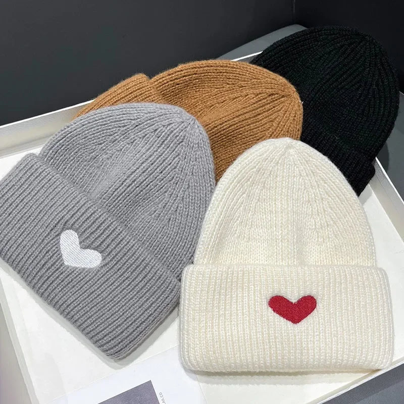 Four Kawaii knit hats in gray, brown, black, and white with heart designs on a white surface.