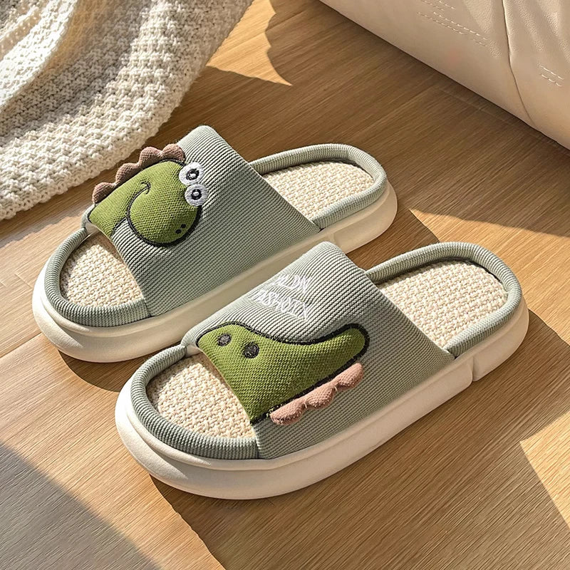 Pair of children's slippers with kawaii dinosaur design on a wooden floor.