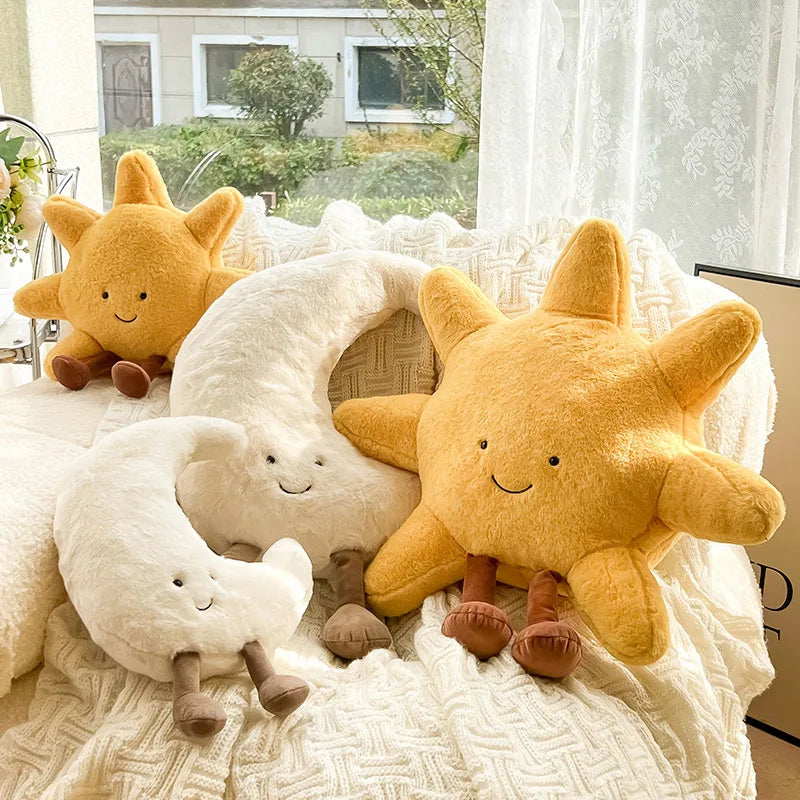 Two kawaii plush suns and a plush moon on a textured surface with a window in the background.