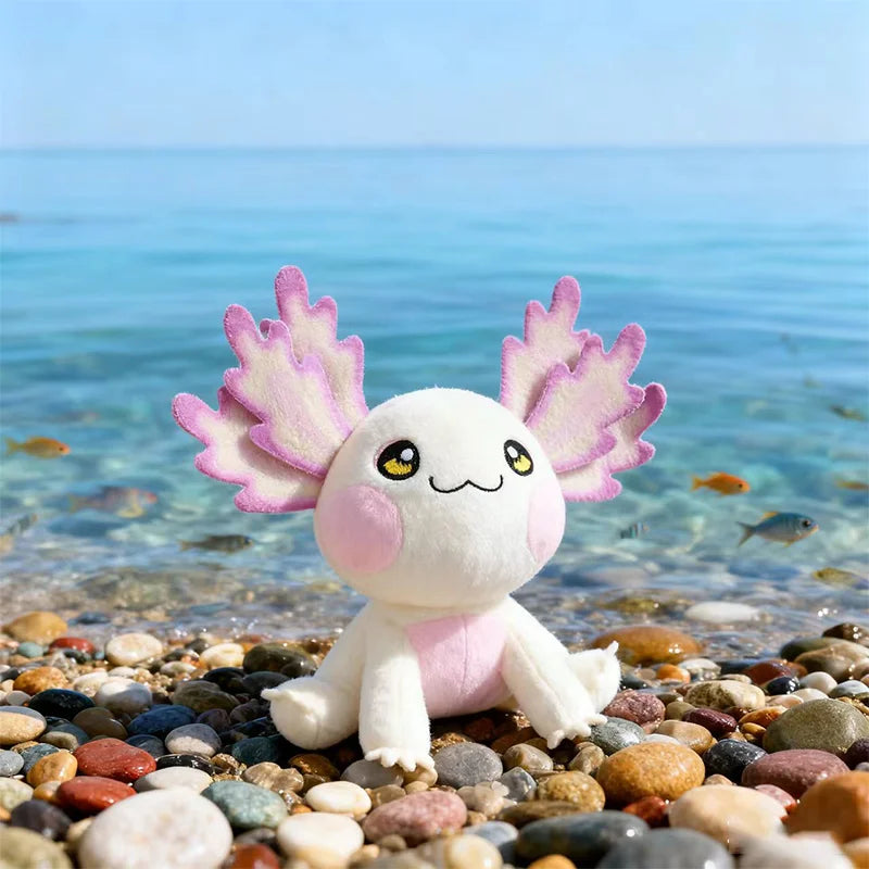 Plush kawaii axolotl toy on pebbles with ocean in the background