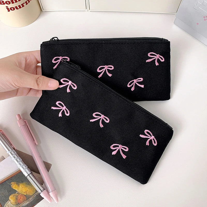 Black kawaii pouch with pink bows held by a hand on a white surface with stationery items.