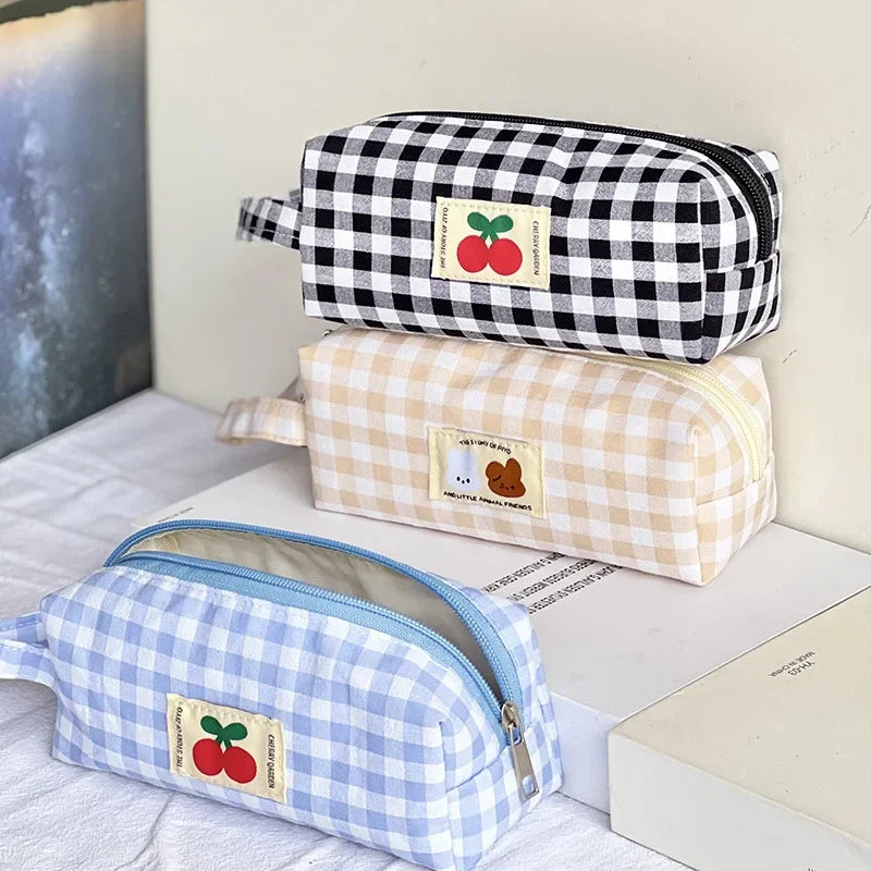 Three checkered kawaii pencil cases with cherry labels on a light surface.