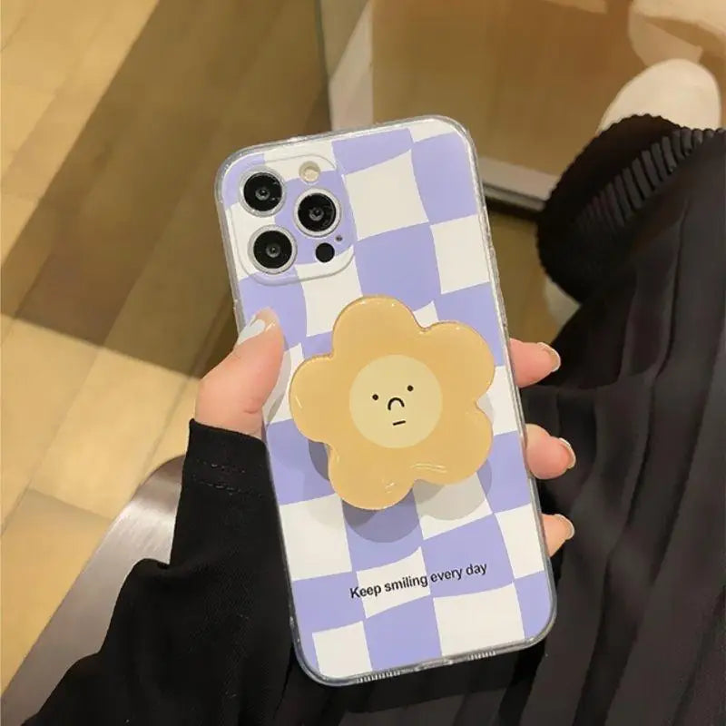 Phone case with a checkered kawaii pattern and cartoon flower design held by a person.
