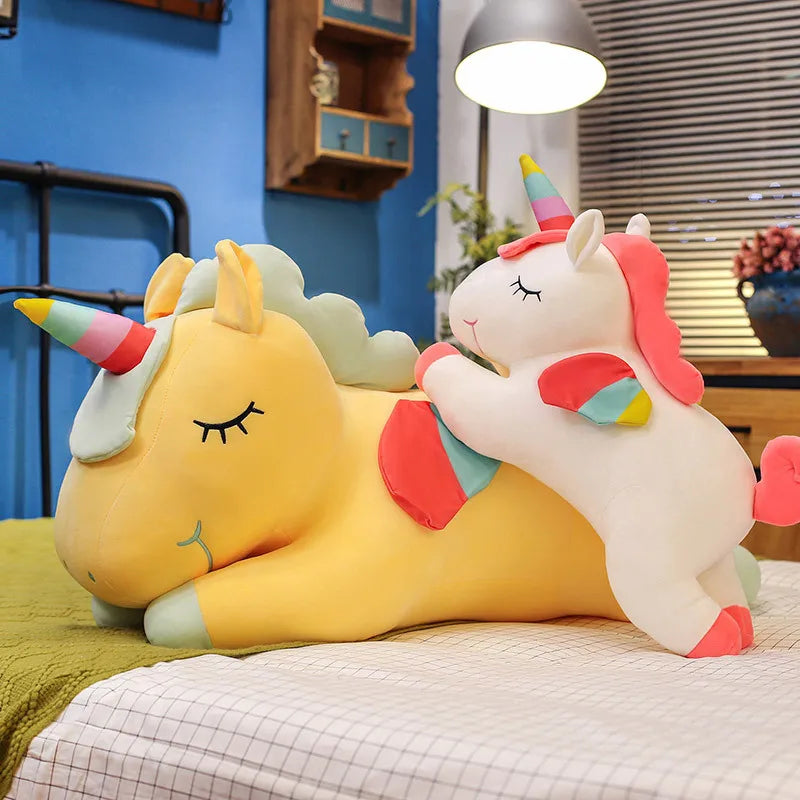 Two colorful unicorn kawaii plush toys on a bed with a blue wall and lamp in the background.