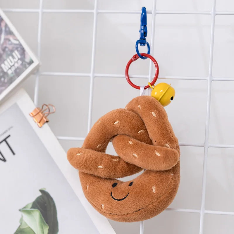 Plush kawaii toy shaped like a pretzel with a smiley face, hanging on a hook against a tiled wall.