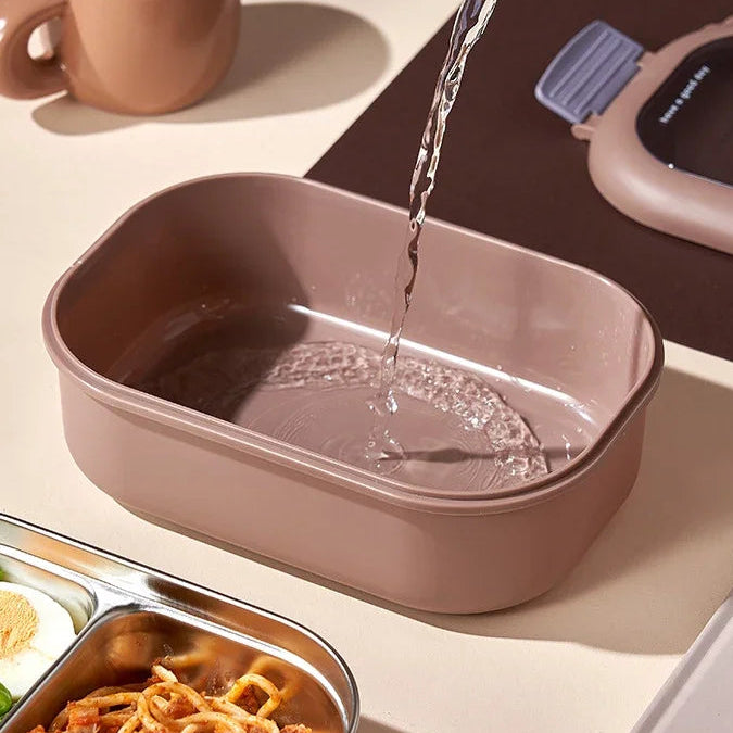 Pink kawaii rectangular container with water being poured into it, next to a cup and food on a beige surface.