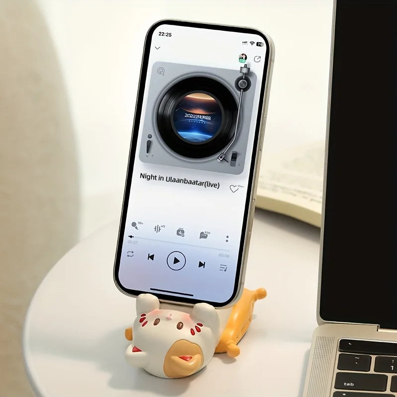 Phone on a kawaii stand with a music app displayed, next to a laptop on a light surface.