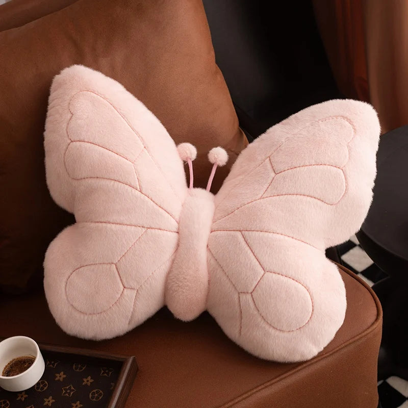 Pink butterfly-shaped kawaii pillow on a brown couch with a cup of coffee in the background.
