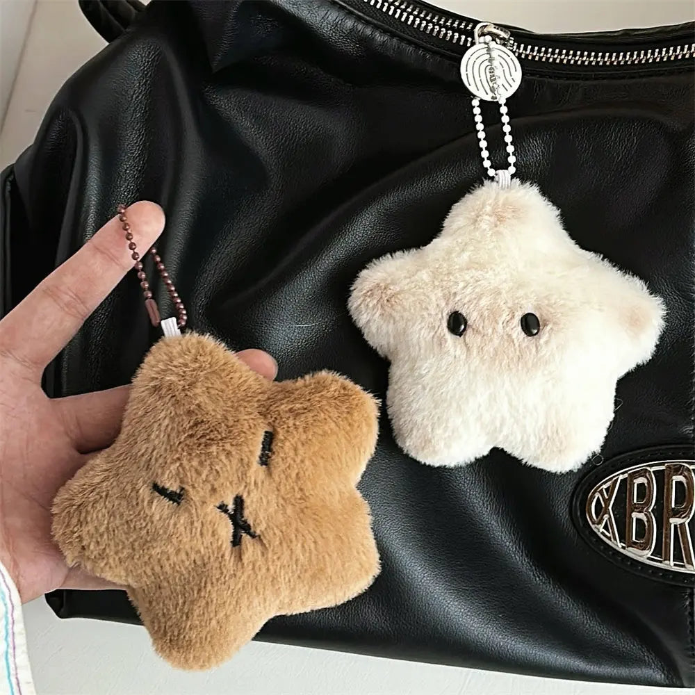 Two plush kawaii keychains, one brown and one white, held against a black leather bag.