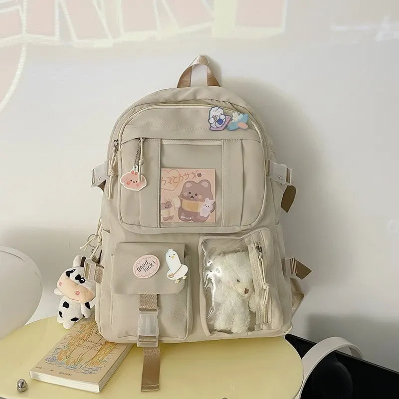 Beige backpack with patches and a small Kawaii plush toy on a light surface.