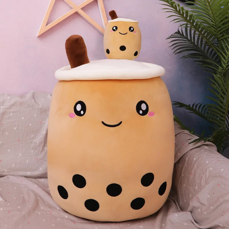 Cute plush kawaii toy resembling a bubble tea cup with a smaller plush toy on top, sitting on a bed.