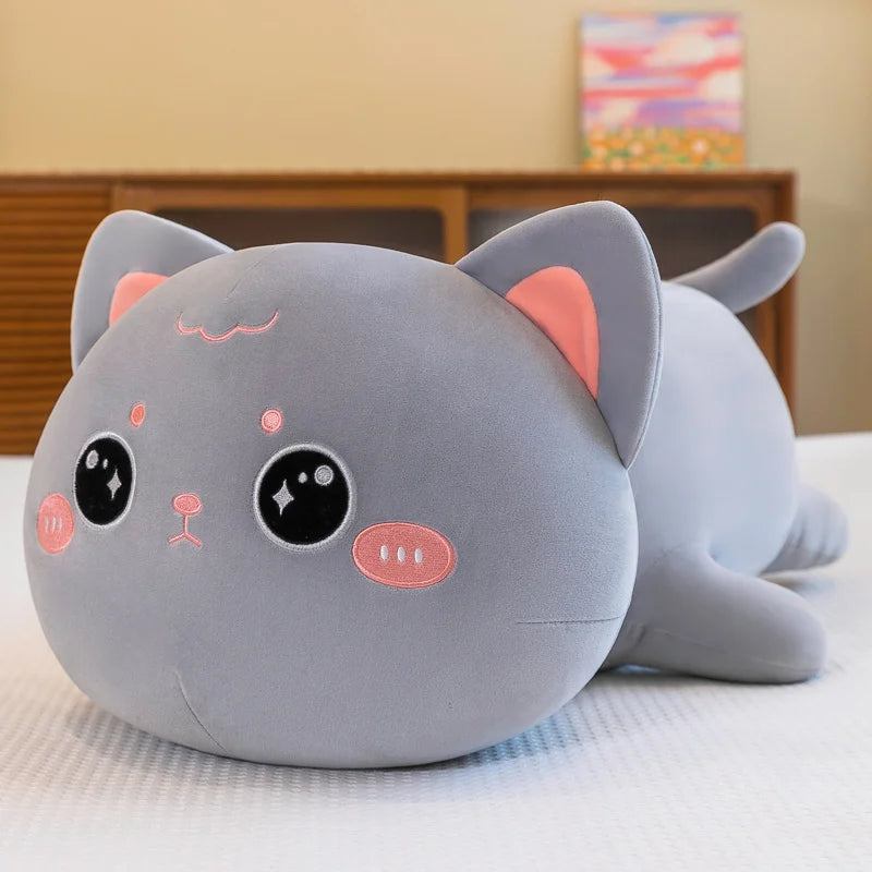 Gray kawaii cat-shaped plush toy on a bed with a blurred background