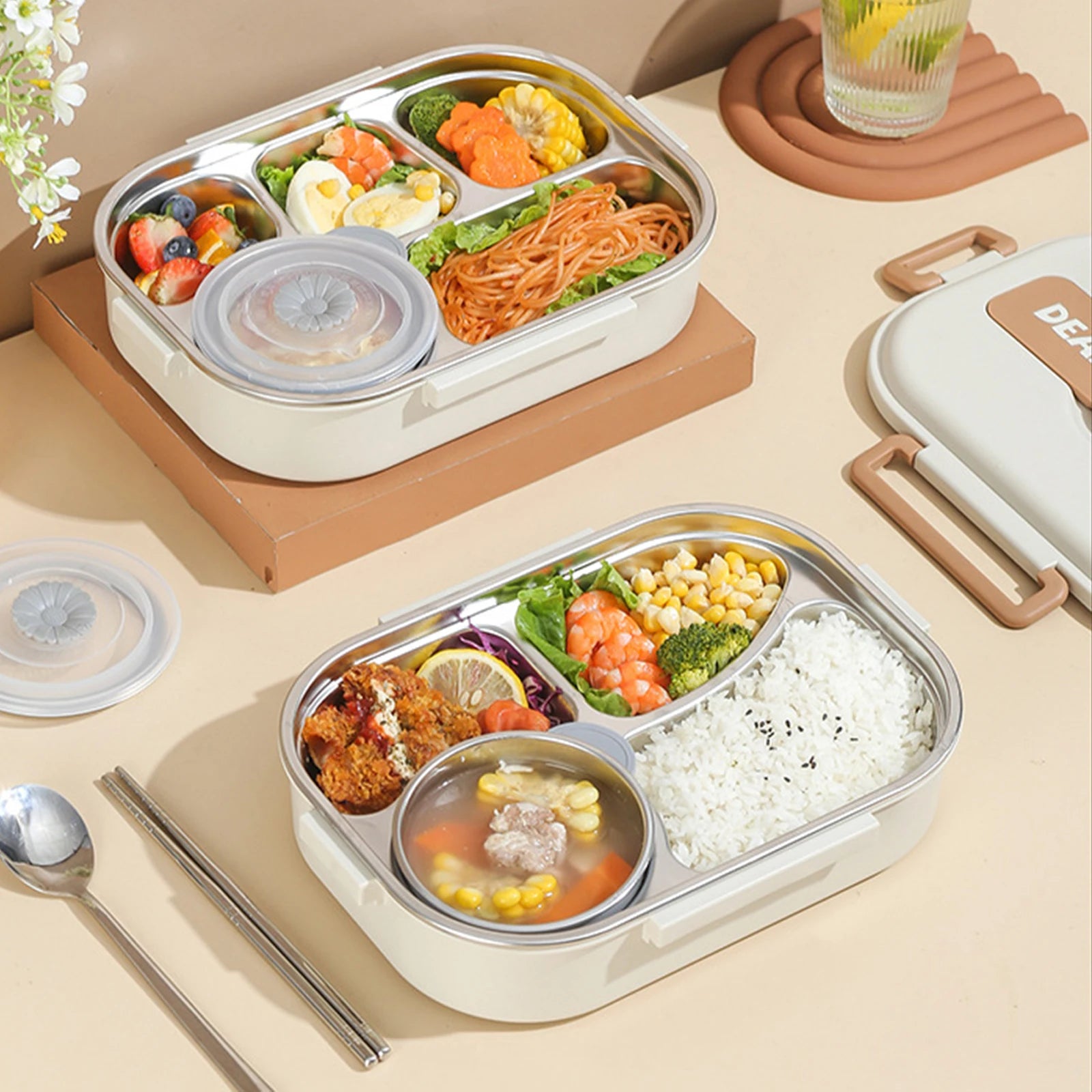 Two kawaii bento boxes with compartments of food on a beige surface with utensils.