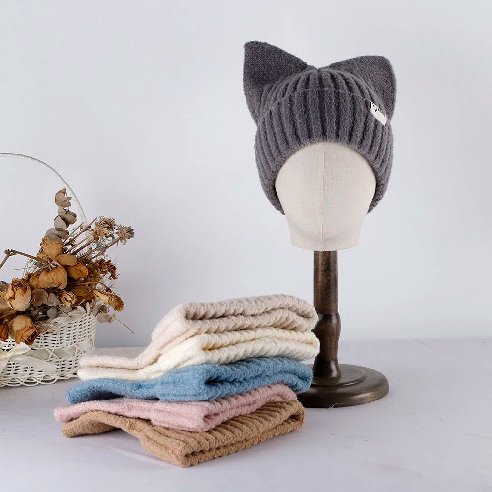 Stack of folded knitted beanies with a gray cat-ear Kawaii hat on a mannequin head against a white background.
