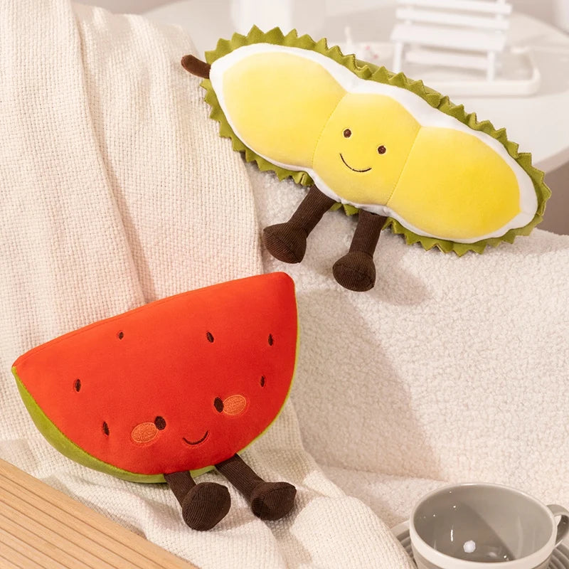 Two plush kawaii toys shaped like a watermelon slice and a peanut on a light fabric background.
