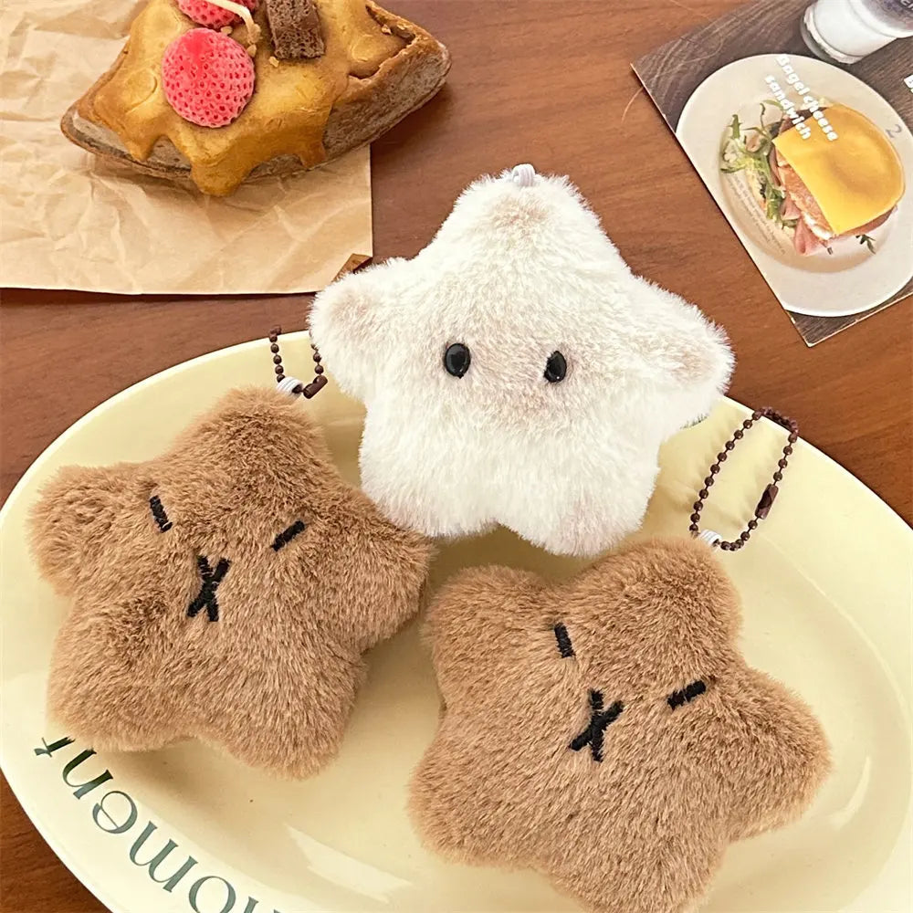 Two kawaii plush keychains, one white and one brown, on a plate with food items in the background.