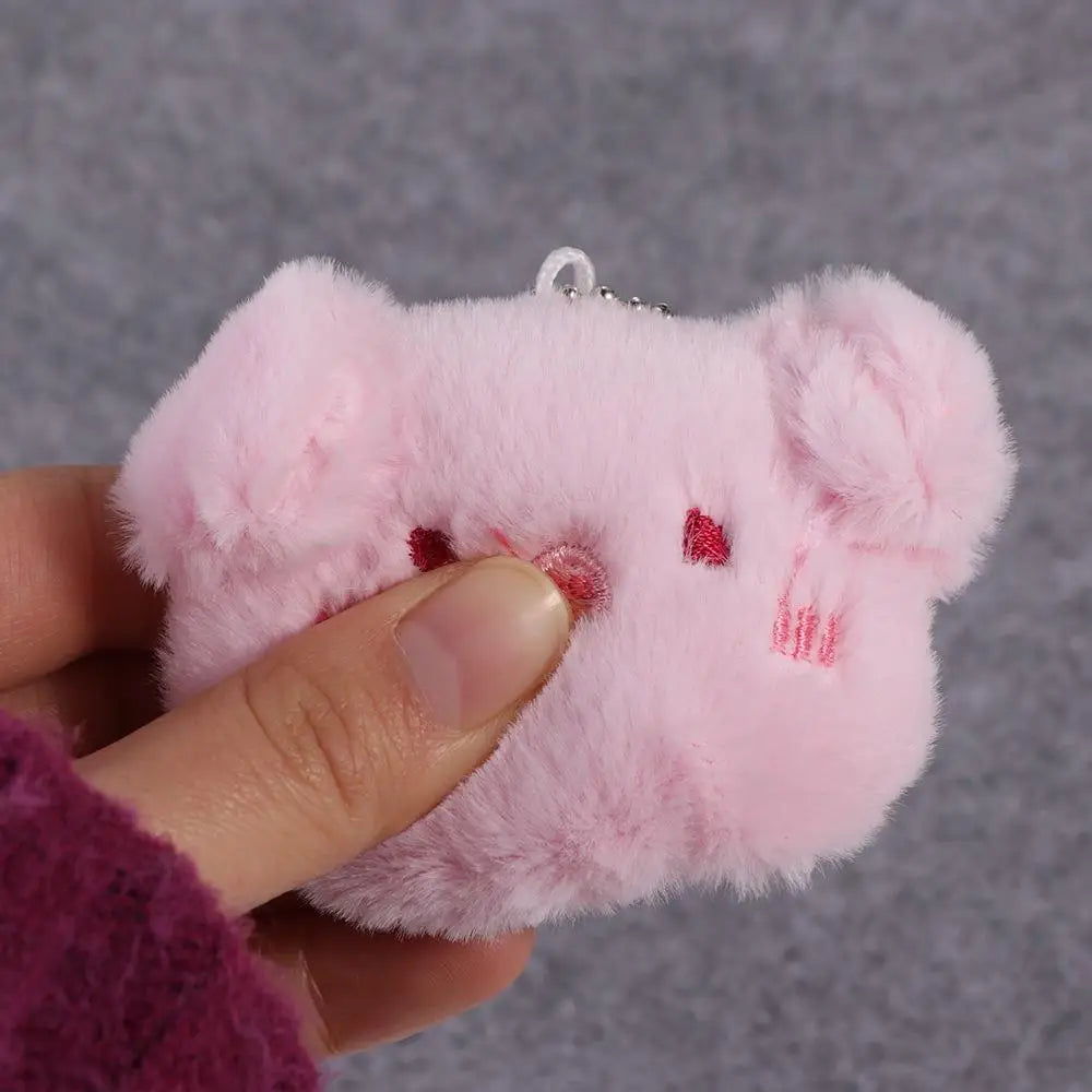 Pink plush kawaii keychain held by a hand against a gray background