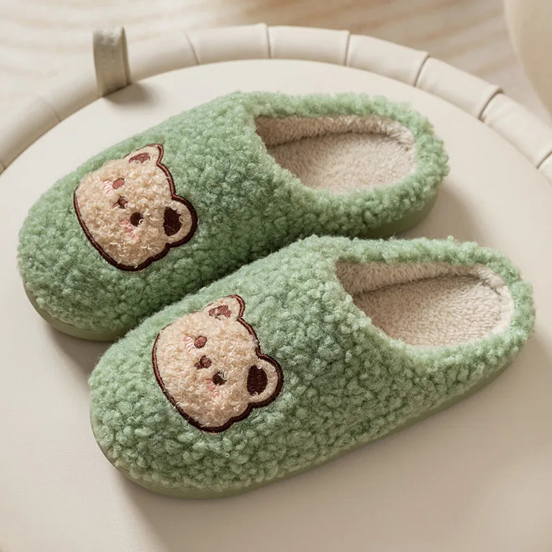 Pair of green slippers with kawaii bear face designs on a light surface