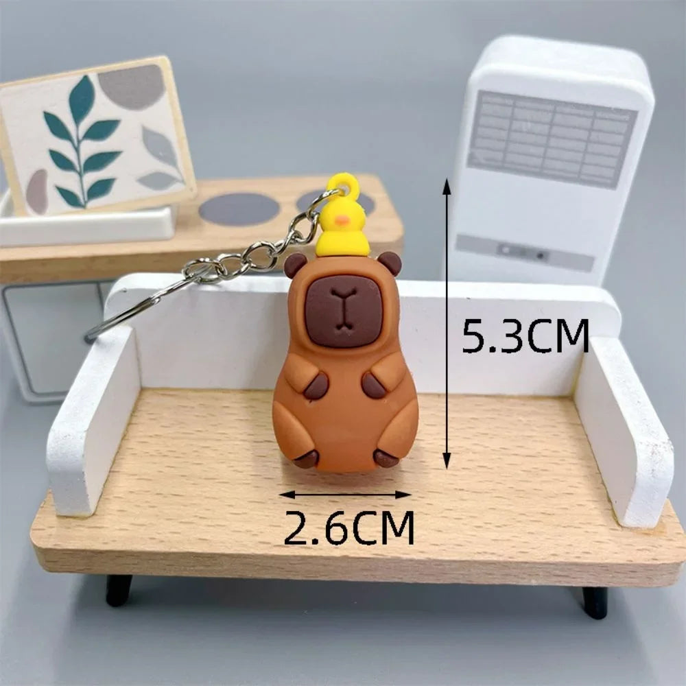 Brown bear-shaped kawaii keychain with a yellow duck on top, displayed on a small wooden desk with measurements indicated.