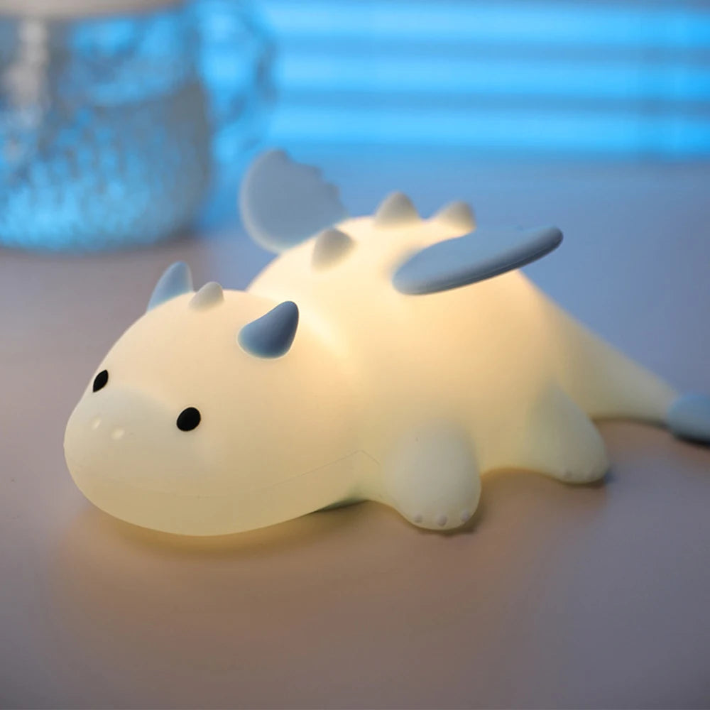 Cute kawaii dragon-shaped night light on a soft surface with a blurred blue background