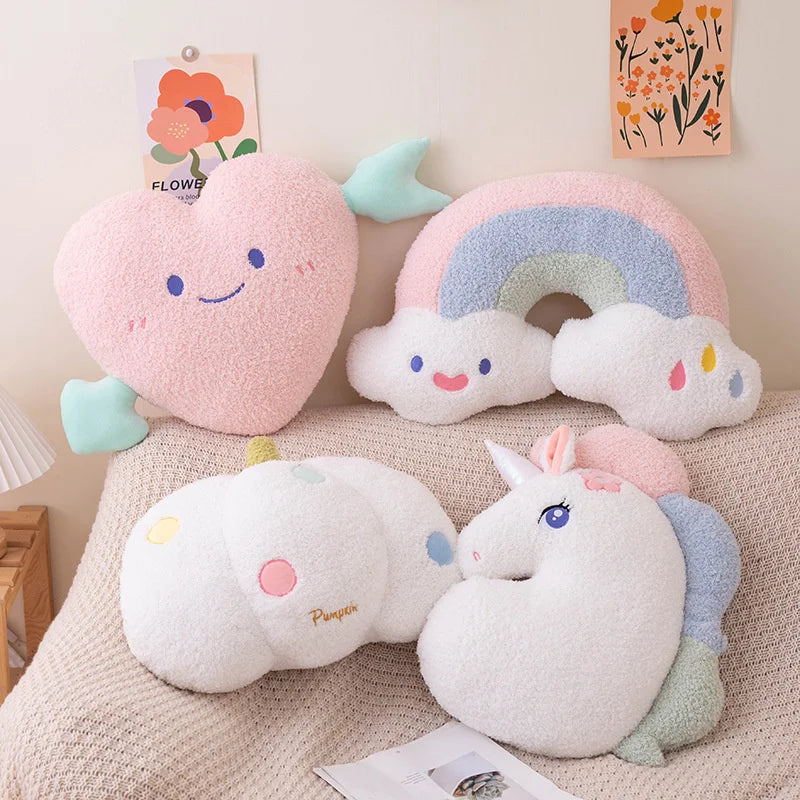 Set of kawaii plush pillows shaped like a cloud, rainbow, and unicorn on a bed.