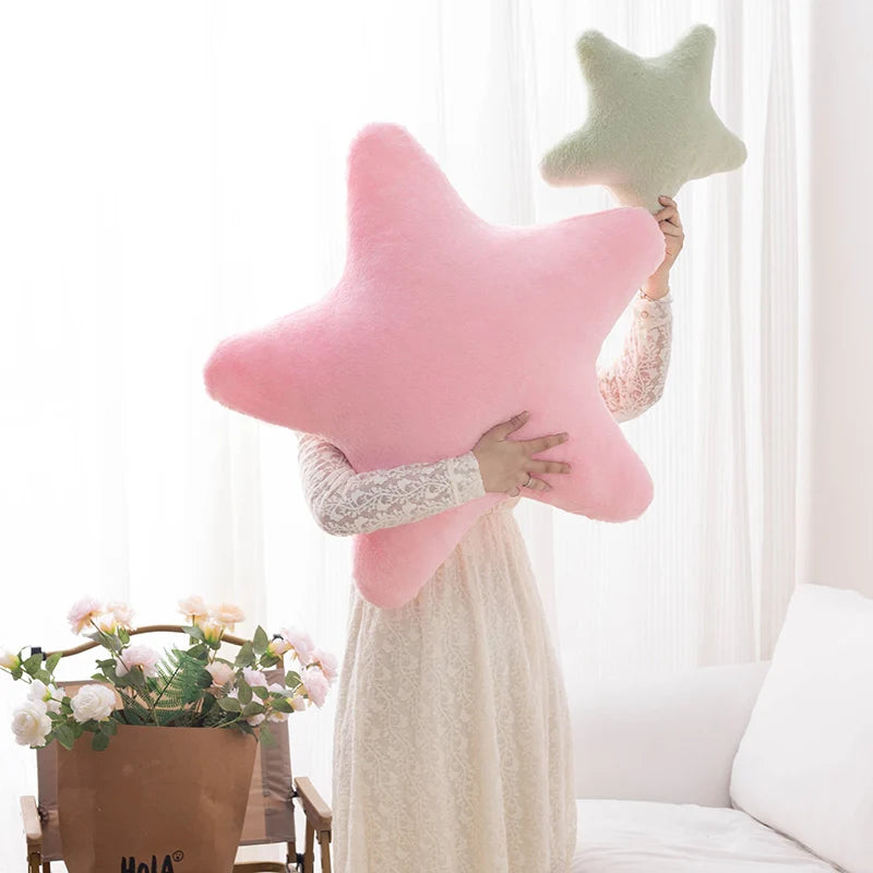 Person holding a pink star-shaped kawaii pillow with another green star-shaped pillow in a bright room.