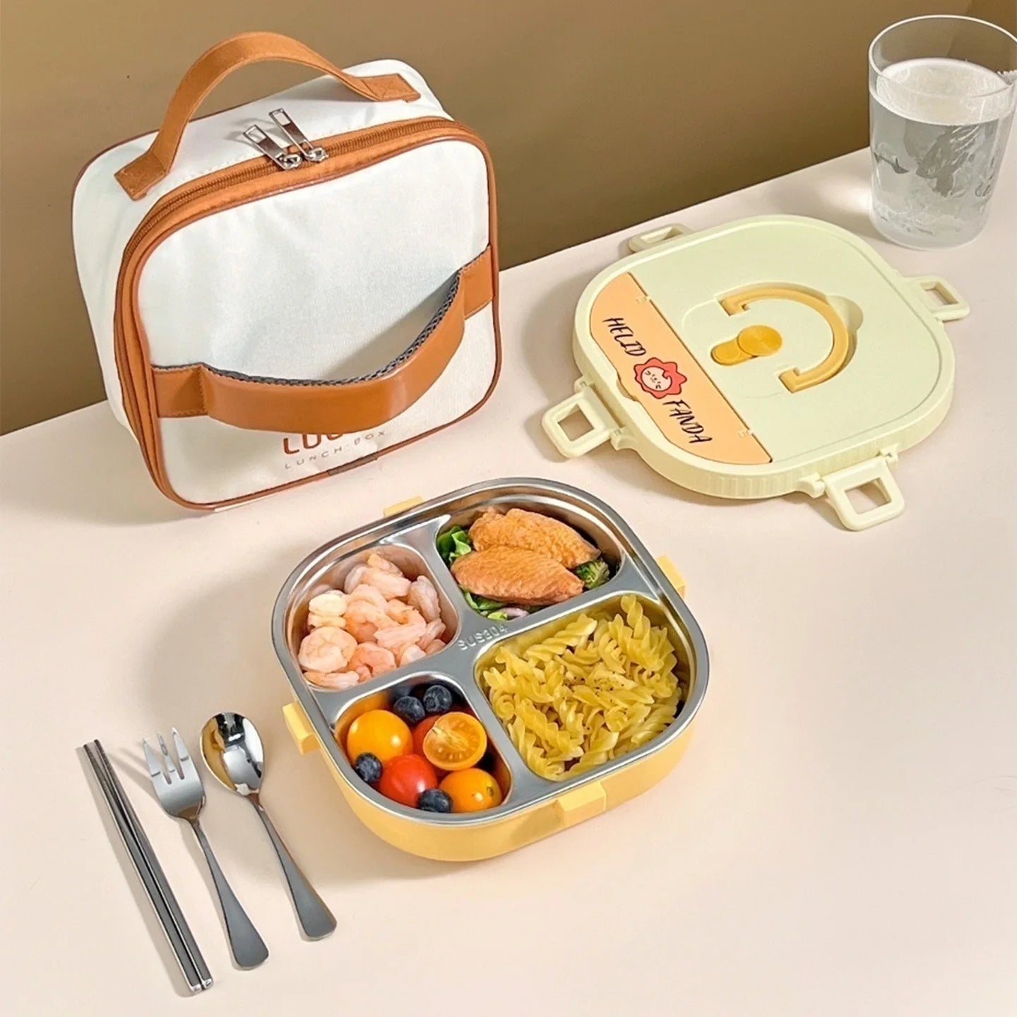 Kawaii lunch box with compartments, fork, spoon, and glass of water on a beige surface.