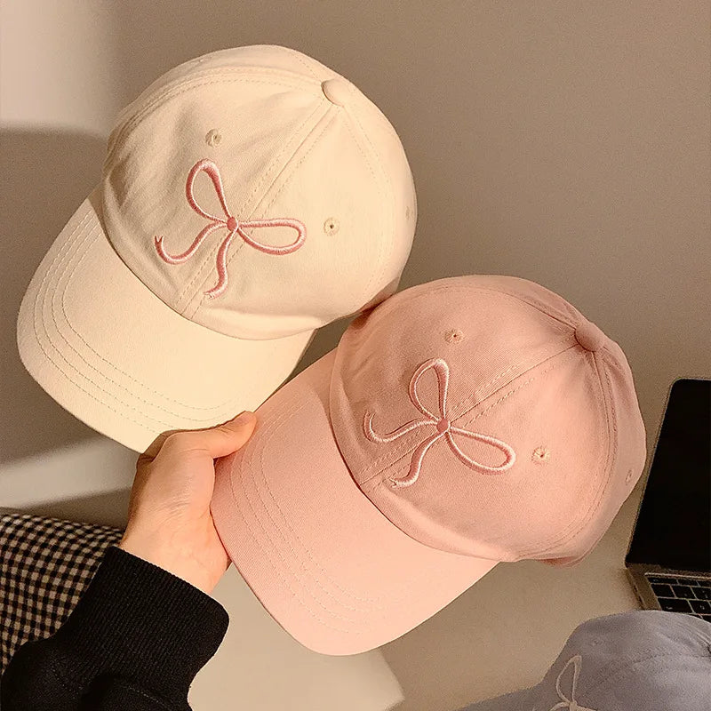 Two Kawaii baseball caps with embroidered designs held by a person against a neutral background.