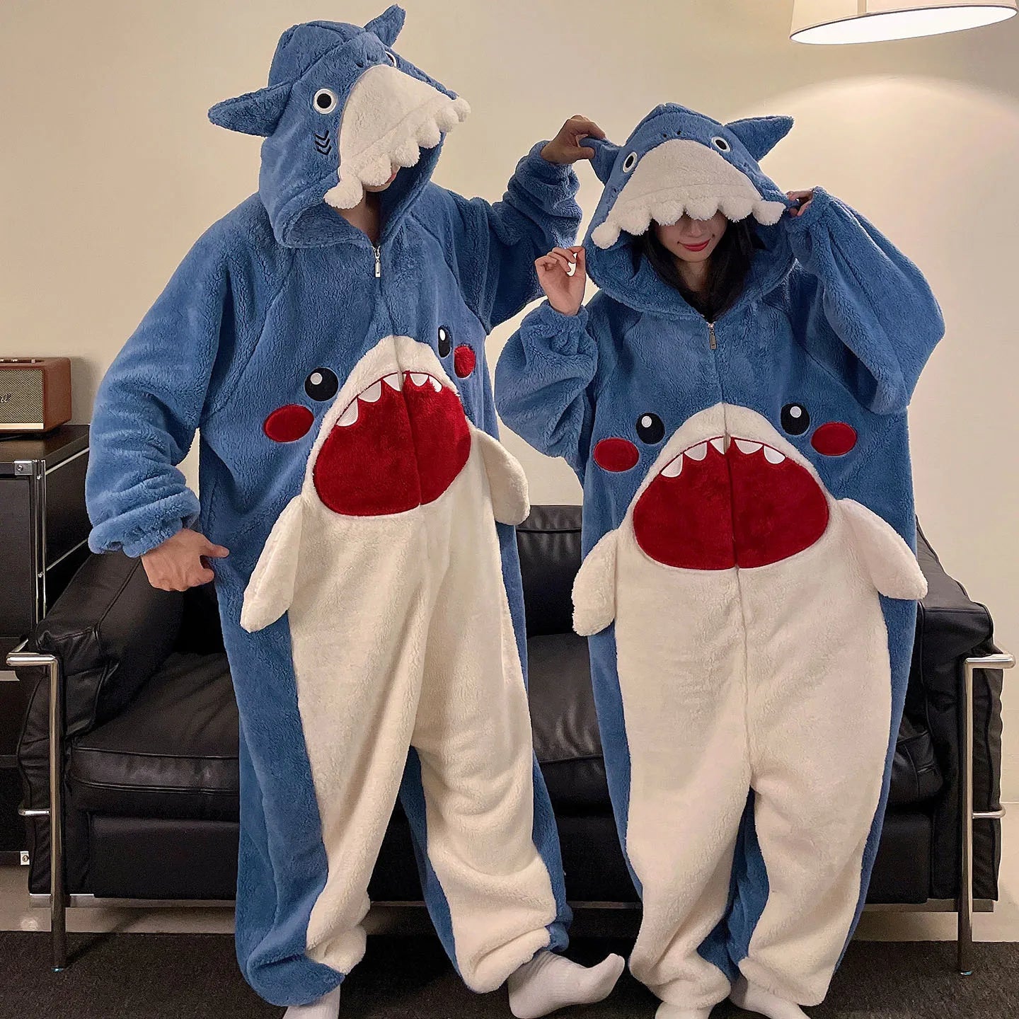 Two people wearing kawaii shark-themed onesies in a living room setting.