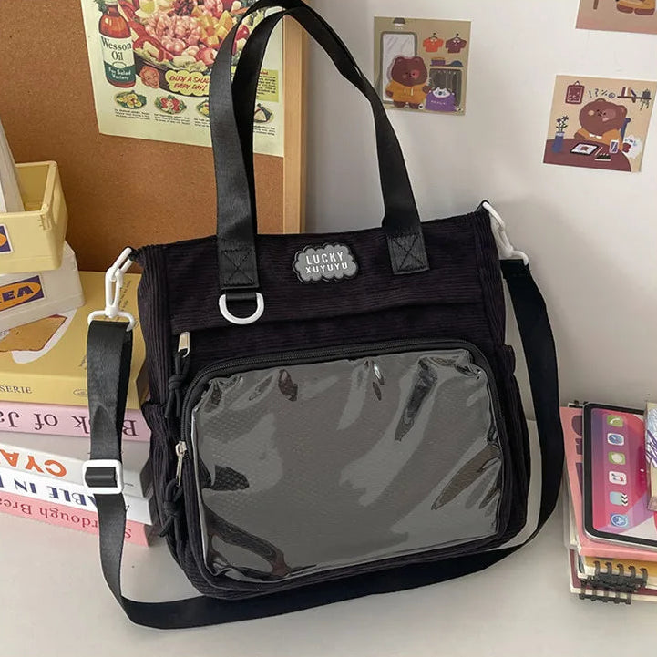 Black Kawaii bag with transparent front pocket on a surface with books and a phone in the background